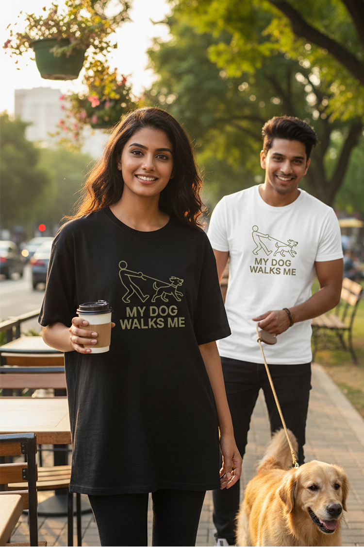 Two people walking a dog in a park with 'My Dog Walks Me' t-shirts.